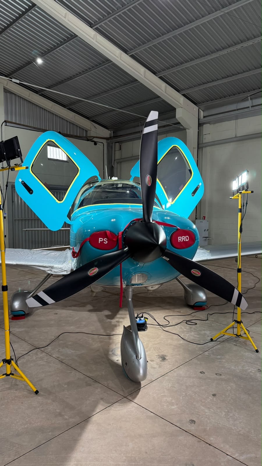Teal single-engine aircraft under detailing lights in the hangar