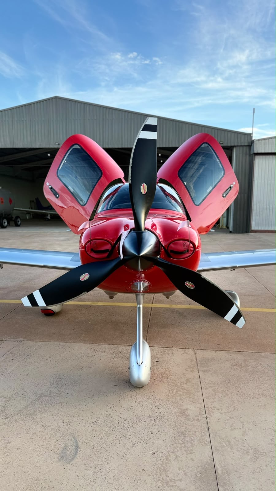 Red single-engine aircraft with gull-wing doors open on the ramp after detailing